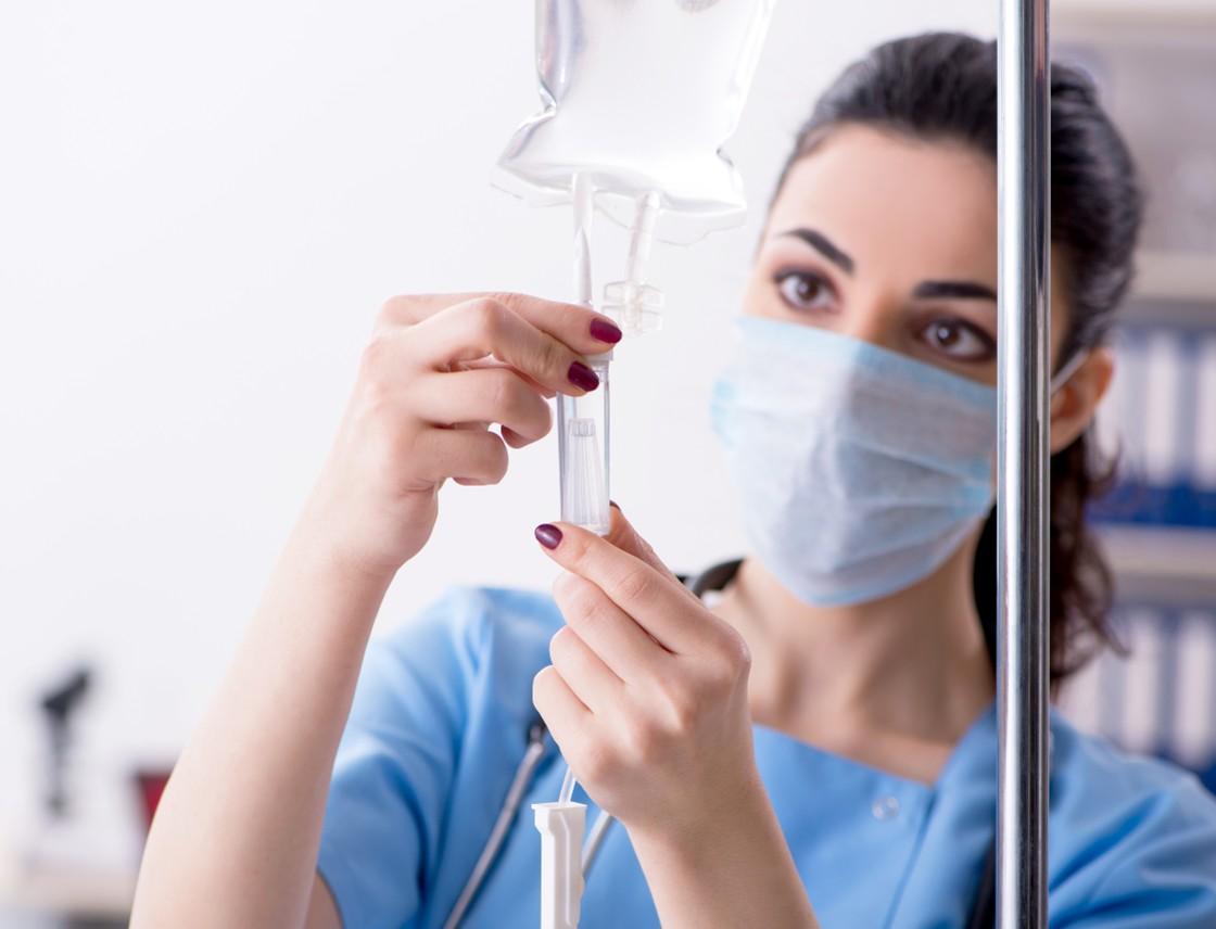 A woman in blue scrubs holding an iv tube.