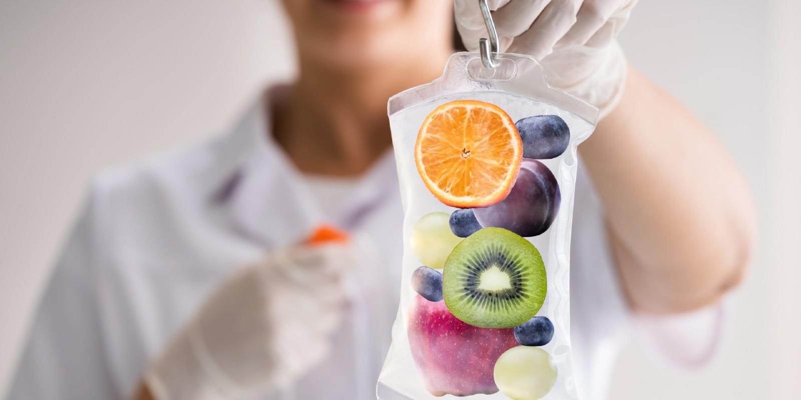 A person holding an orange and kiwi in front of them.