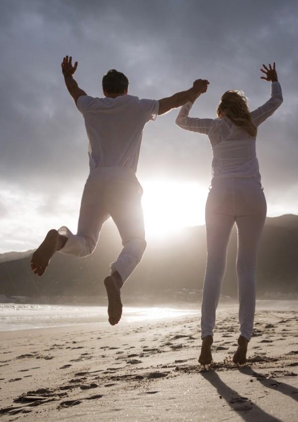 A man and woman jumping in the air on the beach.